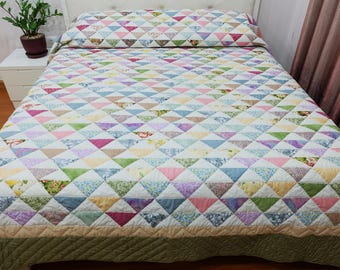 May include: A colorful patchwork quilt and pillow set with a geometric triangle pattern in various pastel colors. The quilt has a cream-colored border and is displayed on a bed. The bedding set is a cozy addition to any bedroom.