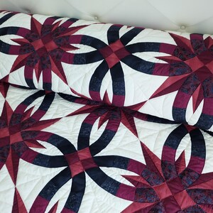 May include: A quilted bedspread and pillow with a repeating pattern of dark red and navy blue interlocking rings and starbursts on a white background. The quilt has a soft, textured appearance.