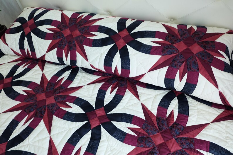 May include: A quilted bedspread and pillow with a repeating pattern of dark red and navy blue interlocking rings and starbursts on a white background. The quilt has a soft, textured appearance.