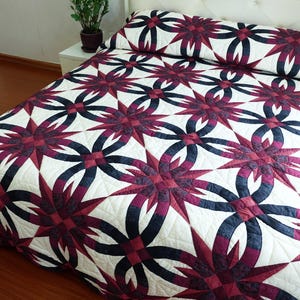 May include: A bed covered with a quilt featuring a repeating pattern of interlocking dark blue and burgundy shapes against a white background. The quilt is on a bed with a white headboard.