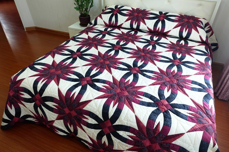 May include: A bed covered with a quilt featuring a repeating pattern of interlocking dark blue and burgundy shapes against a white background. The quilt is on a bed with a white headboard.