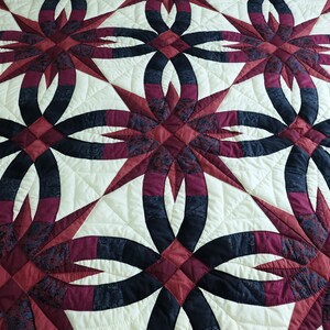 May include: A quilted bedspread with a repeating pattern of interlocking rings and starbursts. The design features burgundy, navy, and cream colors. The quilt is made of fabric and has a textured surface.