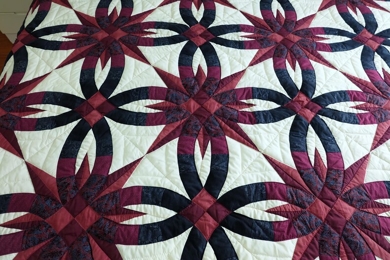 May include: A quilted bedspread with a repeating pattern of interlocking rings and starbursts. The design features burgundy, navy, and cream colors. The quilt is made of fabric and has a textured surface.