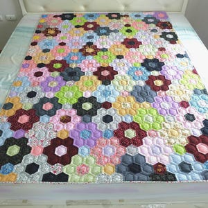 Puede incluir: Un edredón hecho a mano y colorido con un diseño floral. El edredón está compuesto por numerosas formas hexagonales en varios colores, incluyendo rojo, rosa, azul, verde y negro. El edredón está colocado sobre una cama.