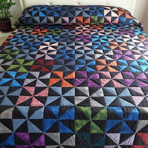 May include: A colorful quilt with a geometric pattern of triangles in shades of blue, green, orange, purple, and pink on a black background. The quilt is on a bed with a matching pillowcase.