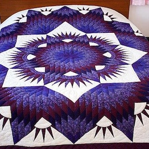 May include: A handmade quilt with a geometric starburst design in shades of purple, white, and burgundy. The quilt is on a bed, showcasing the intricate patchwork and quilting details. The overall theme is home decor.
