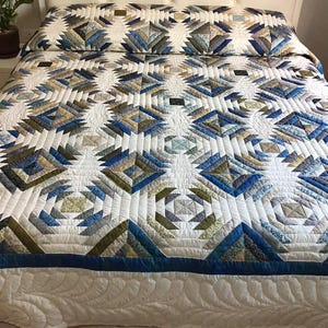 Può includere: Una trapunta da letto con un motivo geometrico a blocchi di ananas in tonalità blu, verde oliva e marrone chiaro, su sfondo bianco. La trapunta presenta un'intricata trapuntatura a macchina e un bordo bianco solido con un disegno a piuma.