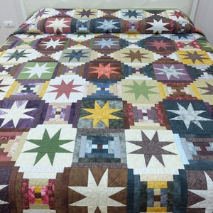 May include: A colorful quilt with a star pattern, displayed on a bed. The quilt features a patchwork design with various colors, including white, green, brown, purple, and yellow. The star shapes are prominent throughout the design.
