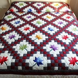 May include: A colourful quilt featuring a repeating pattern of red and white squares, and white squares with multi-coloured floral designs. The quilt is on a bed, and the colours include red, white, blue, green, yellow, and purple.
