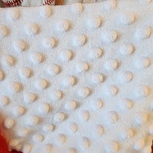 May include: A white, textured fabric with raised, circular dots is visible, along with a red felt base. Baseball-themed fabric with baseballs and mitts is at the top. The image suggests a sports-themed item.