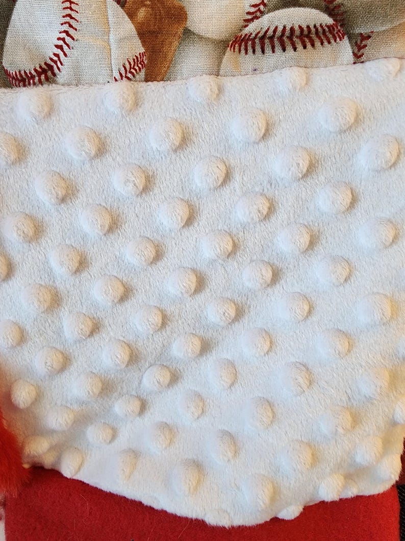 May include: A white, textured fabric with raised, circular dots is visible, along with a red felt base. Baseball-themed fabric with baseballs and mitts is at the top. The image suggests a sports-themed item.