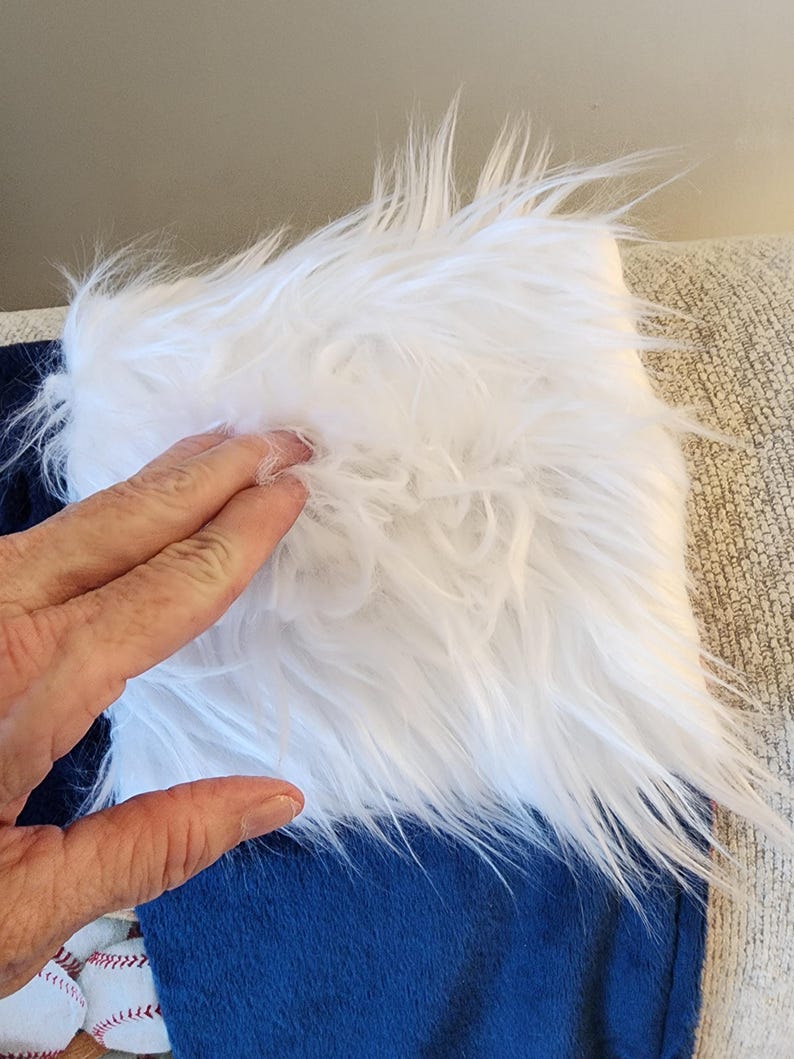 May include: A close-up of a blue and white baseball stocking. The top portion is white faux fur, and the bottom is blue fabric. Baseball-themed decorations are visible at the bottom of the stocking.
