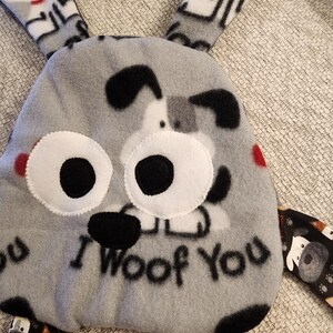 May include: A gray plush dog toy with the text "I Woof You". The toy has large white eyes with black pupils, black ears, and red accents. The toy has multiple patterned fabric appendages.