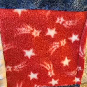 May include: Close-up of a patchwork textile featuring a red fleece panel with white stars and shooting star designs. The panel is bordered by blue and denim fabrics, creating a patriotic theme.