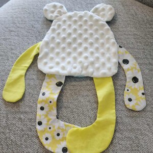 Może przedstawiać: Ręcznie robiona zabawka dla dziecka w kształcie misia. Miś ma białą, teksturowaną głowę z dwoma małymi uszami. Ręce i nogi są ż&oacute;łte i wzorzyste z białymi stokrotkami i czarnymi środkami. Zabawka jest przeznaczona dla dzieci.