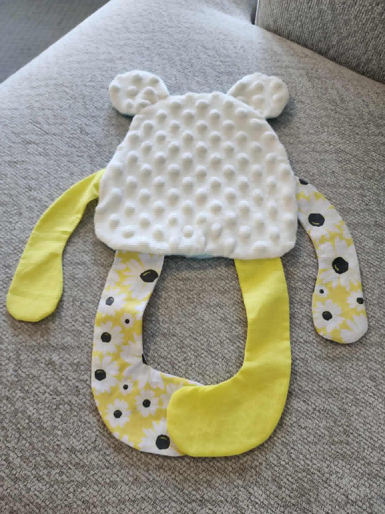 Może przedstawiać: Ręcznie robiona zabawka dla dziecka w kształcie misia. Miś ma białą, teksturowaną głowę z dwoma małymi uszami. Ręce i nogi są ż&oacute;łte i wzorzyste z białymi stokrotkami i czarnymi środkami. Zabawka jest przeznaczona dla dzieci.