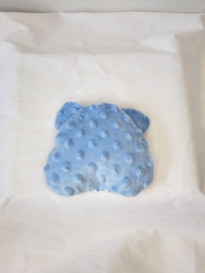 May include: A light blue, plush baby blanket with a textured, dotted surface. The blanket is a soft, cloud-like shape, perfect for a baby's comfort. The blanket is made of a soft, fuzzy material.