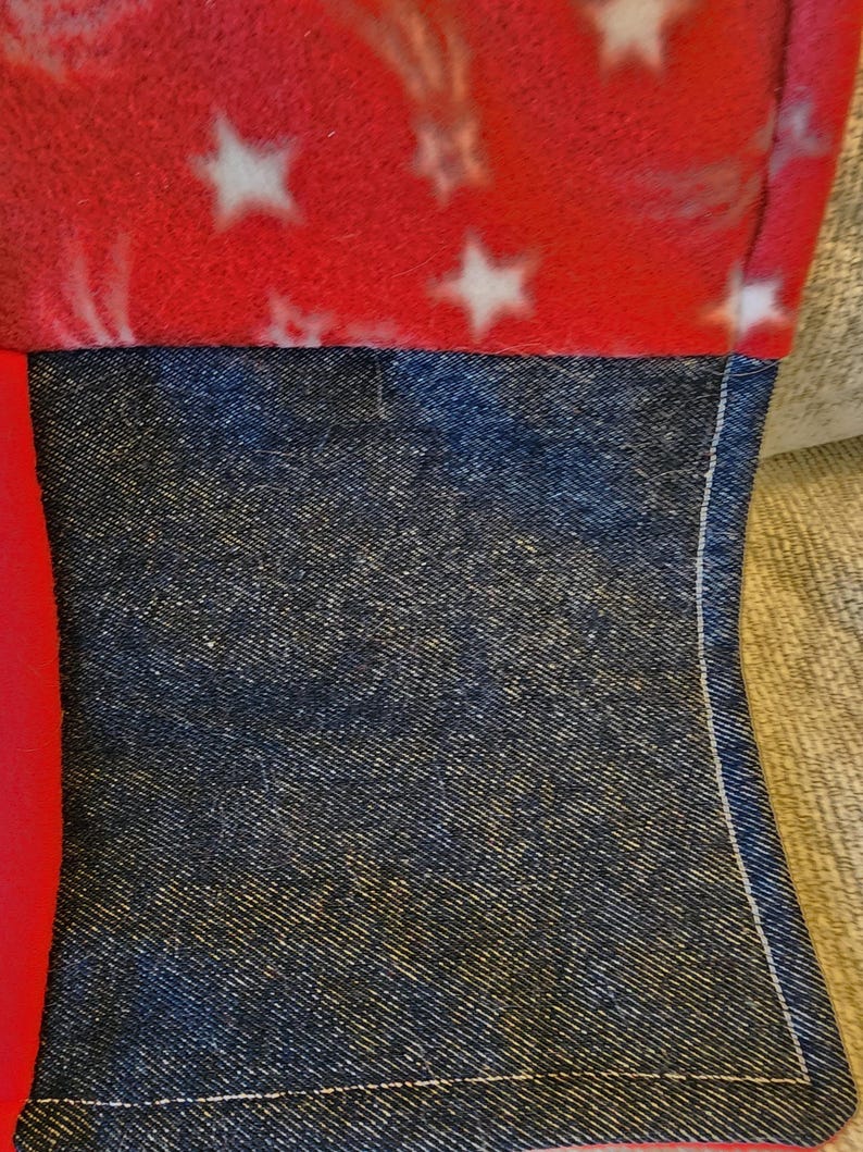 May include: Close-up of a section of a sewn item. The top portion is red fleece with white stars. Below is a section of dark blue denim fabric. The two fabrics are sewn together with white thread.