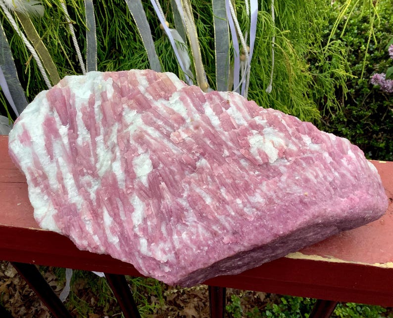 May include: A large, raw mineral specimen featuring a striking combination of vibrant pink and opaque white crystalline structures. The stone displays a rough, textured surface with elongated, parallel formations throughout the entire piece.