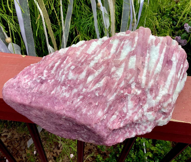 May include: A large, raw mineral specimen featuring a striking combination of vibrant pink tourmaline crystals embedded within a white quartz matrix. The stone displays a rough, natural texture with elongated, vertical crystal formations throughout.