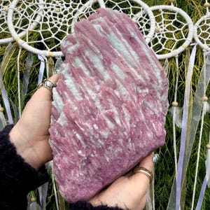 May include: A large, raw mineral specimen featuring a striking combination of vibrant pink and pale white crystalline structures. The stone displays a vertical, striated texture throughout its surface, showcasing natural formations and jagged edges.