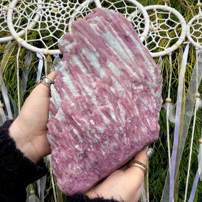 May include: A large, raw mineral specimen featuring a striking combination of vibrant pink and pale white crystalline structures. The stone displays a vertical, striated texture throughout its surface, showcasing natural formations and jagged edges.