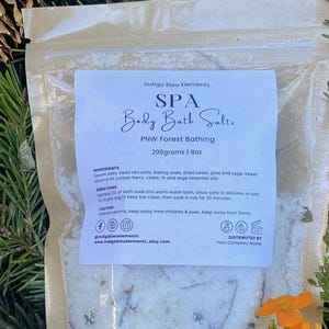 May include: A white bag with a label that reads "Indigo Bleu Elements SPA Body Bath Salts PNW Forest Bathing 200grams | 8oz". The label also includes ingredients, directions, and a caution statement. The bag is filled with white bath salts.
