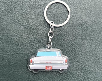 May include: A silver car keychain featuring the rear view of a classic sedan with a light blue rear window, red taillights, and a red license plate displaying the number 92100. The keychain includes a silver metal split ring and chain.