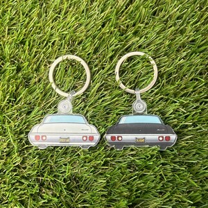 以下が含まれることがあります： クラシックカーの後部をモチーフにしたキーホルダー2個セット。1つは「POST 48」のナンバープレートが付いた白いキーホルダー、もう1つは「2LIGHT」のナンバープレートが付いた黒いキーホルダーです。