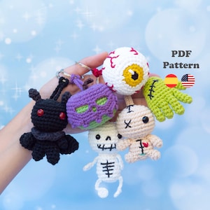 Puede incluir: Una colección de cinco llaveros de ganchillo que incluyen una criatura negra con ojos rojos, una calavera morada, un globo ocular blanco con venas rojas, un esqueleto blanco y una mano verde. El texto PDF Pattern es visible junto a banderas.