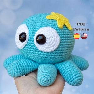 Puede incluir: Un pulpo azul tejido a ganchillo con grandes ojos con borde blanco y una estrella amarilla en la cabeza. El pulpo tiene ocho tentáculos azules. La imagen incluye el texto "PDF Pattern" y banderas.