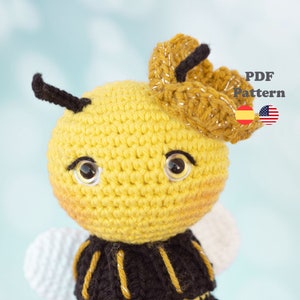 Puede incluir: Un juguete de amigurumi de abeja tejido a crochet con un cuerpo amarillo, rayas negras y una flor marrón en la cabeza. La abeja tiene ojos grandes y marrones y una antena negra.