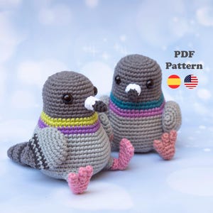 May include: Two handmade crochet pigeon toys. The birds are grey with colourful accents around their necks and pink feet. One bird is sitting, and the other is slightly behind it. The text "PDF Pattern" is in the upper right corner.