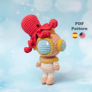 Puede incluir: Una muñeca amigurumi de ganchillo vestida con un traje de buceo de aguas profundas beige y blanco con una visera de casco azul claro y detalles amarillos, con un pequeño pulpo rojo sobre el casco. El texto PDF Pattern aparece a la derecha.