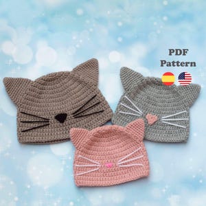 Puede incluir: Tres gorros de gato de ganchillo en tonos marrón, gris y rosa. Cada gorro presenta orejas puntiagudas, bigotes negros o blancos y una nariz en forma de corazón. Los gorros se muestran sobre un fondo azul claro con el texto "PDF Pattern".