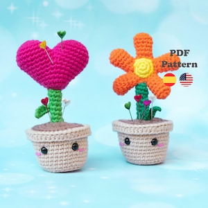 May include: Two crocheted plant figures. One is a pink heart with green stem and leaves, the other is an orange flower with a yellow centre and green stem. Both are in beige pots with smiling faces. The image includes the text "PDF Pattern".