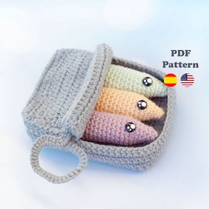 May include: Crochet pattern for a grey tin of sardines with three colourful crocheted fish inside. The pattern is available in both Spanish and English.
