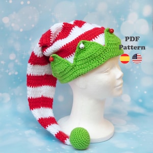 Peut inclure: Un chapeau d'elfe crocheté à la main avec un long sommet pointu rayé rouge et blanc. Le chapeau présente une couronne verte avec des accents rouges et blancs et une boule verte. Le texte "PDF Pattern" est visible.