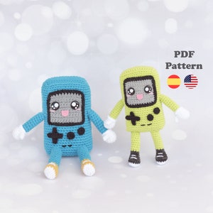 Puede incluir: Dos peluches de crochet con forma de consolas de videojuegos portátiles. Una es azul y la otra es verde. Ambas tienen caras sonrientes con ojos grandes y una lengua rosa que sobresale.  Patrón PDF.