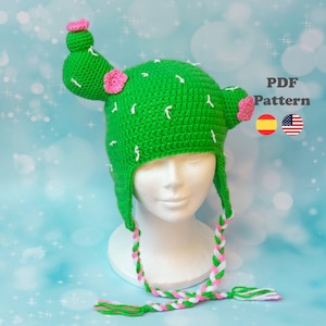 Peut inclure: Patron de chapeau cactus au crochet en format PDF. Le patron est disponible en anglais et en espagnol. Le chapeau est vert avec des fleurs roses et des accents blancs. Le chapeau a un long cordon tressé.