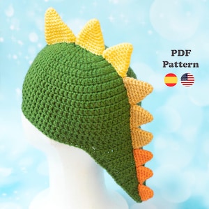 May include: A green crochet hat with yellow, orange, and tan accents, designed to resemble a dinosaur. The hat features a row of triangular spikes down the back and top. The text "PDF Pattern" is visible.