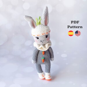 Puede incluir: Patrón de amigurumi de crochet para un conejito gris que lleva un gorro blanco con hojas verdes y un cuello de volantes naranja. El conejito sostiene dos zanahorias naranjas. El patrón está disponible en español e inglés. Patrón PDF.