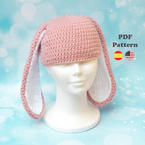 May include: A pink crochet bunny hat with long, floppy ears. The inside of the ears is white, contrasting with the pink exterior. The hat is displayed on a white mannequin head. The text "PDF Pattern" is visible.