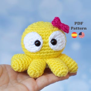 May include: A crocheted yellow octopus with white eyes and a pink bow. The octopus has eight yellow tentacles. The text "PDF Pattern" is visible in the image, along with the flags of Spain and the United States.