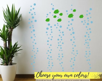 May include: Wall decal featuring a design of blue bubbles and green fish. The text "Choose your own colors!" is displayed on a yellow banner. A potted plant is in the corner.