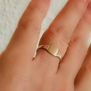May include: A gold signet ring with a smooth, oval-shaped top. The ring is worn on a finger.