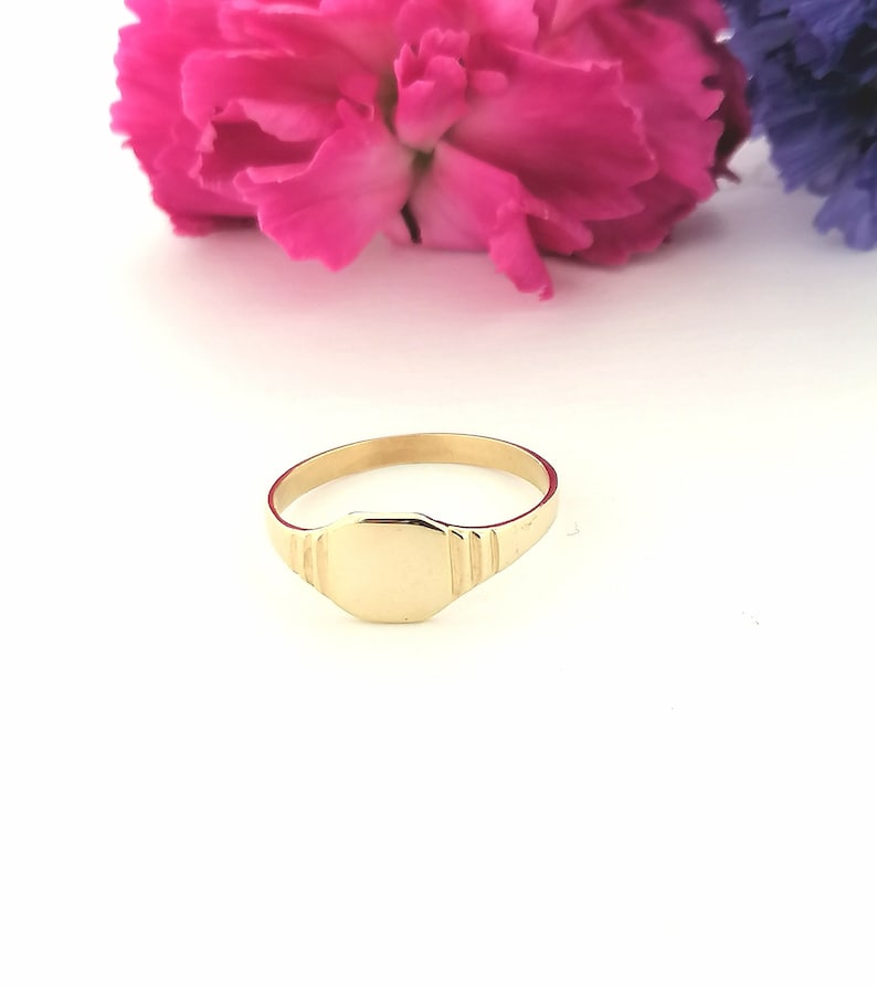 May include: A gold signet ring with a smooth, flat top. The ring has a simple, classic design.