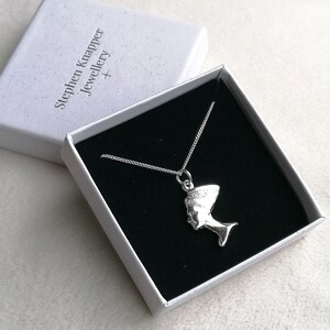 May include: A silver necklace with a pendant shaped like the profile of an Egyptian queen wearing a headdress. The necklace is in a white box with the text "Stephen Knapper Jewellery +" printed on the lid.