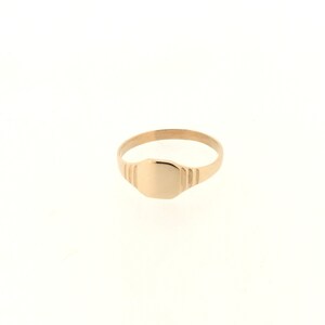 May include: A gold signet ring with a smooth, oval-shaped top. The band of the ring has a textured design.