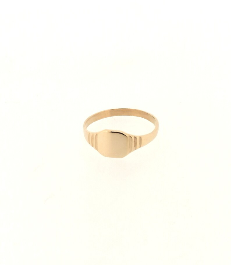 May include: A gold signet ring with a smooth, oval-shaped top. The band of the ring has a textured design.